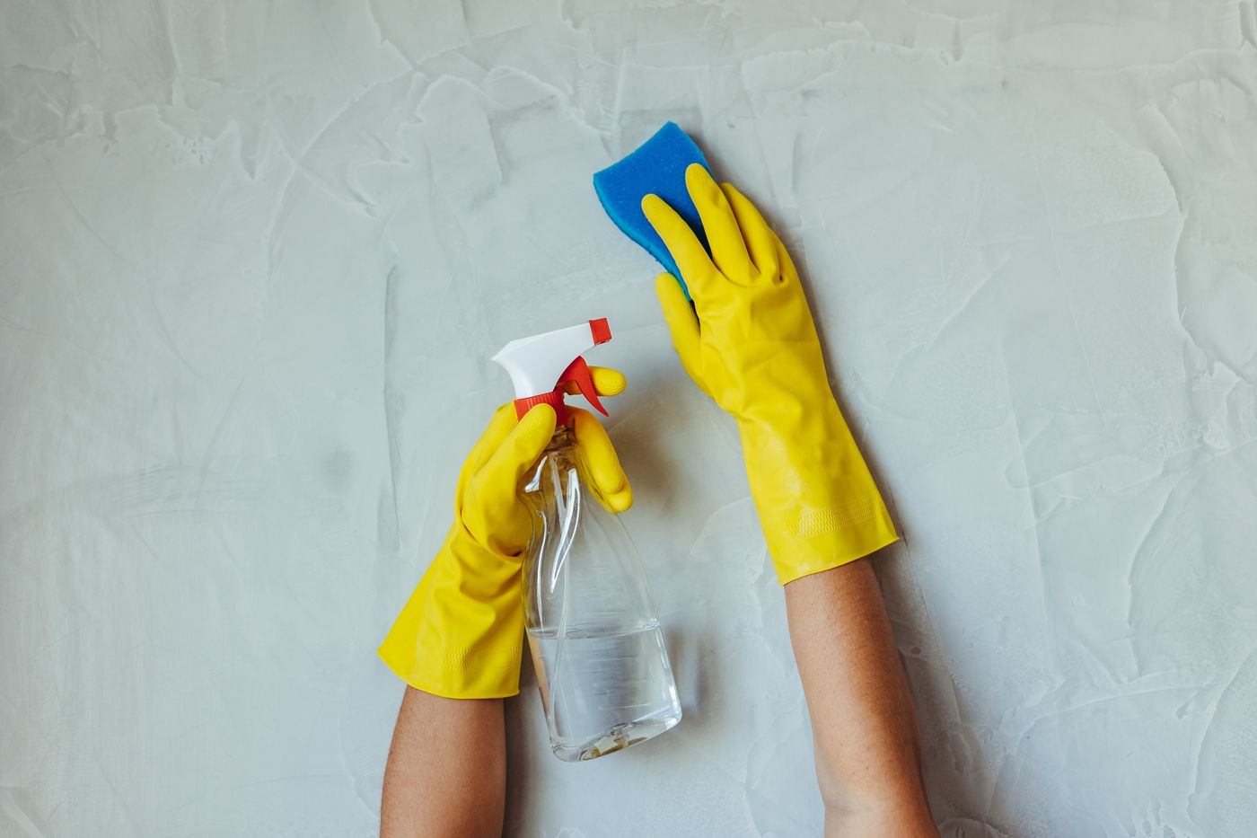 Gloved hands cleaning a wall with a spray bottle and sponge